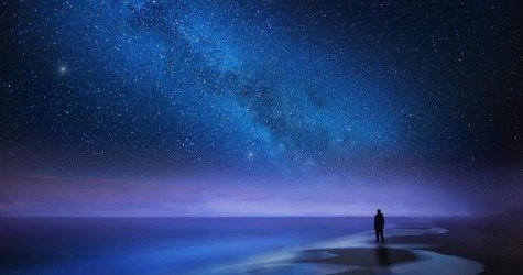 Starry night sky over sea and beach with man silhouette